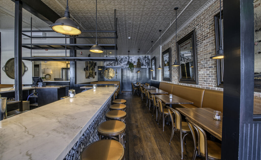 The full length of the bar, with a stone top, industrial pendants and exposed steel glass racks above