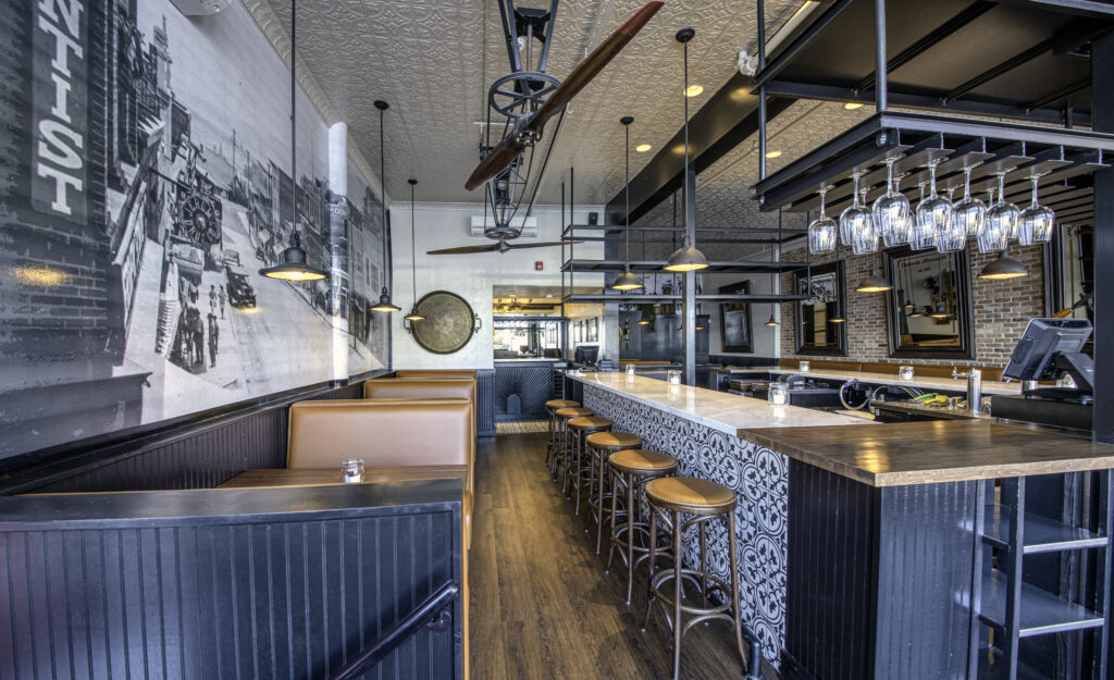 Bar room with a pressed tin ceiling, leather booth seating and a stone-topped bar set on patterned tile