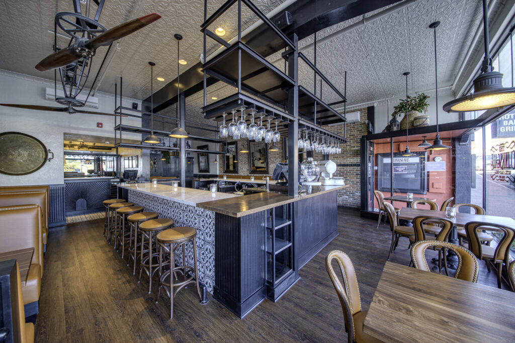 View across the bar to the front doors, with bentwood chairs, cafe tables and a vintage ceiling fan