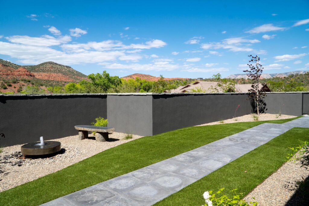 Side lawn running between paving and gravel, with red rock beyond the wall