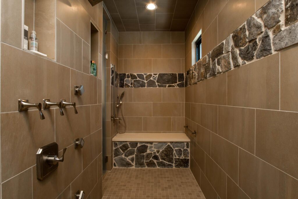 Walk-in shower tiled with a band of stone and a bench along the end