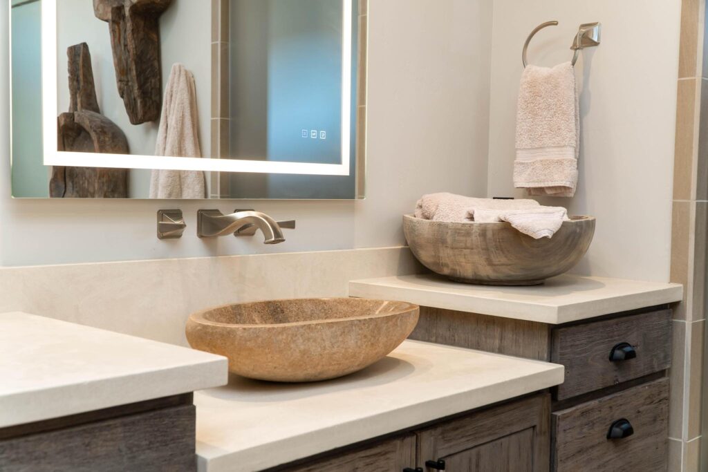 Stone vessel basin set on the counter below a lit mirror
