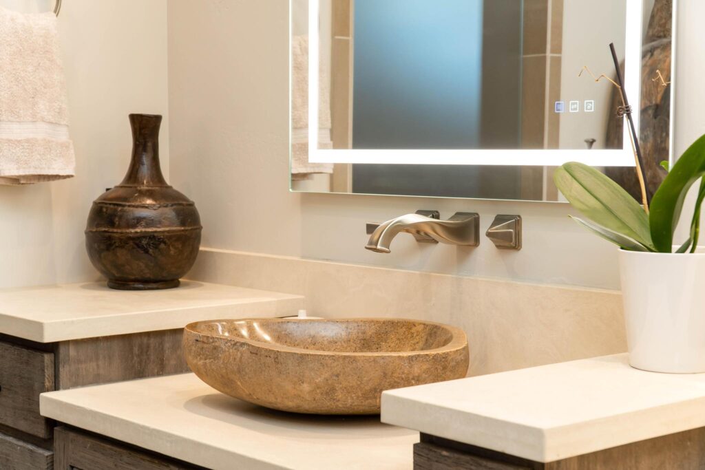 Stone vessel basin on a stepped counter below a lit mirror