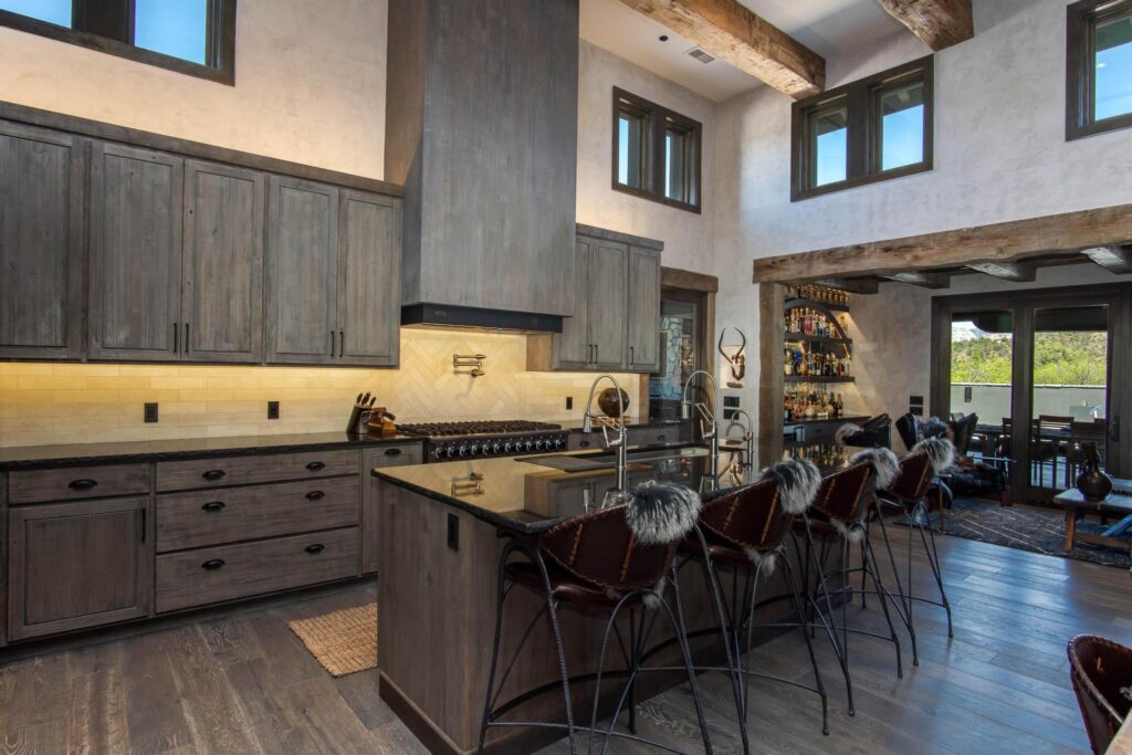 Kitchen with stained cabinetry, stone counters and stools at the island