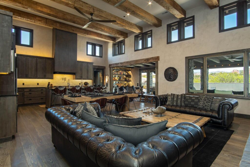 Great room under hewn timber beams, leather seating open to the kitchen beyond