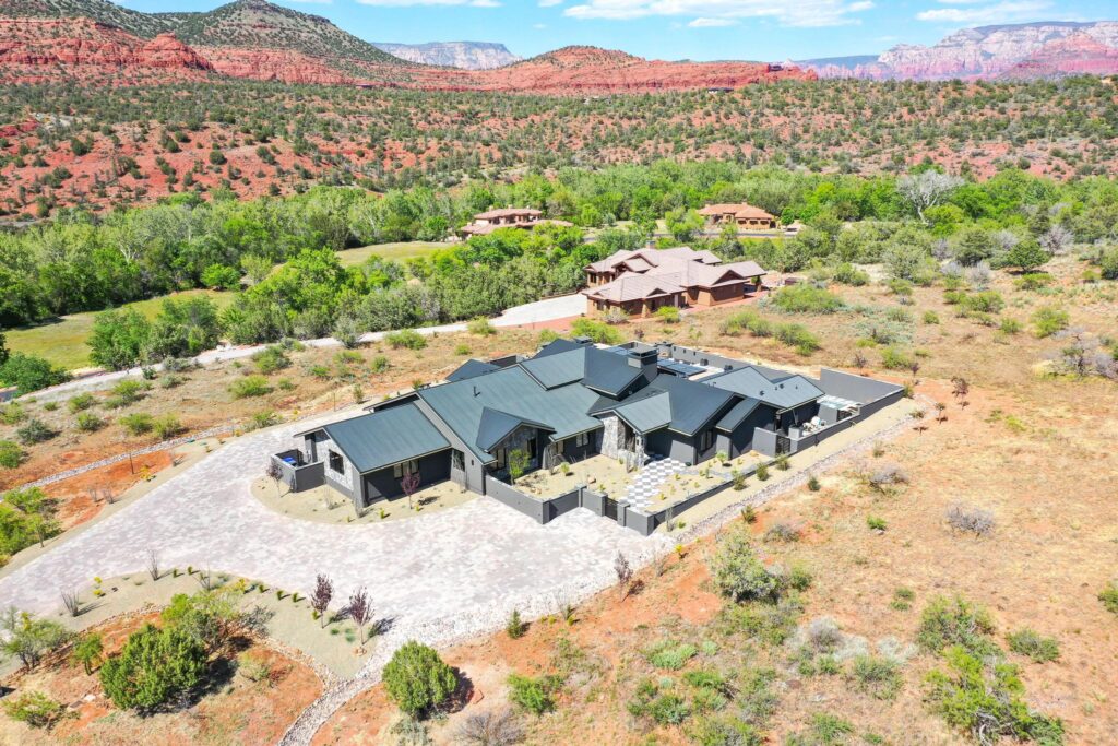The house from the air, low and dark against the desert with red rock behind