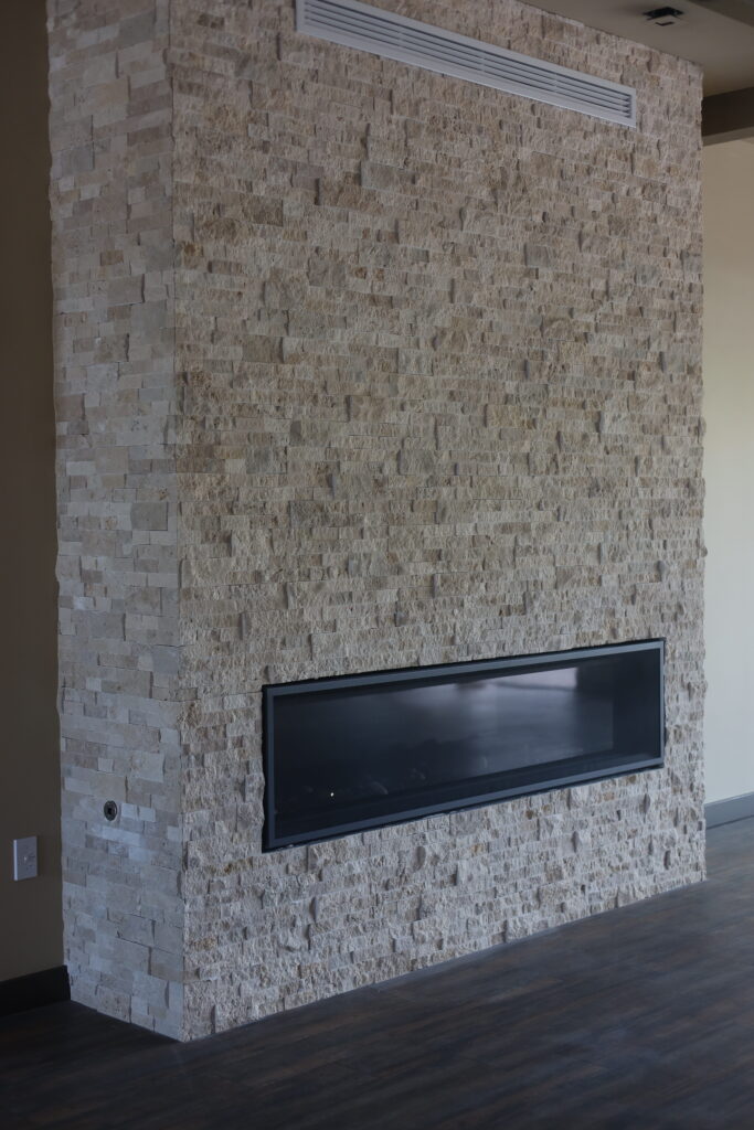 Stacked stone fireplace wall with a linear gas fire, photographed during construction