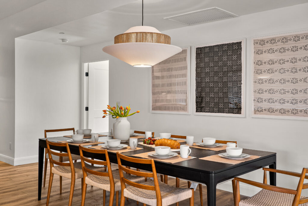 Dining table set for six under a pendant light, with framed textile art on the wall behind