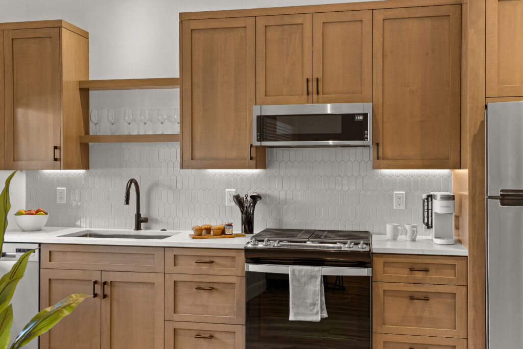 Kitchen with light-toned shaker cabinets, a white tile backsplash, undercabinet lighting, and stainless appliances