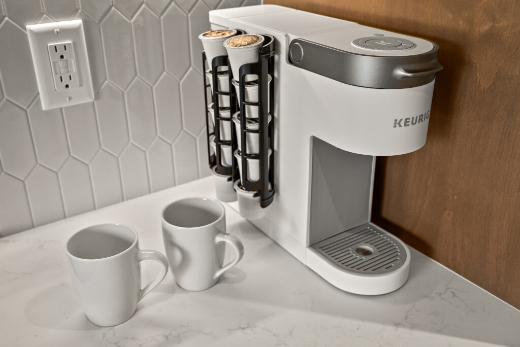 Single-serve coffee maker and two mugs on the counter against a white picket-tile backsplash