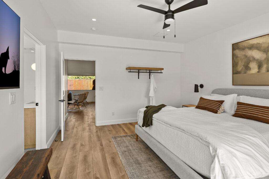 Bedroom looking through to a second room, with a ceiling fan and wide-plank flooring