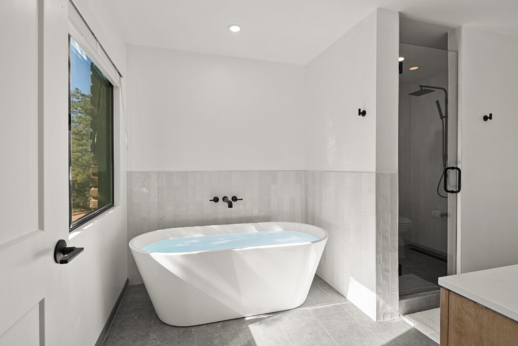 Bathroom with a freestanding soaking tub beside a glass shower and a window to the trees
