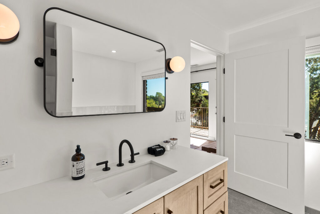 Bathroom vanity with an undermount sink, a wide black-framed mirror, and wall sconces