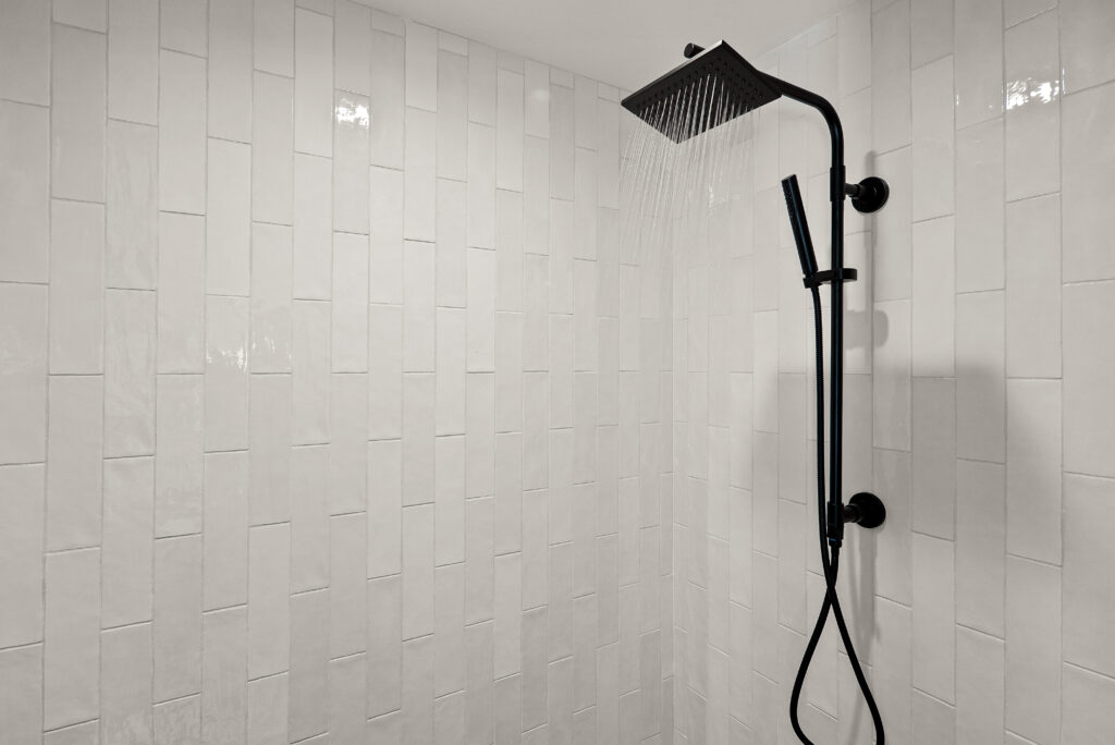 Walk-in shower with vertically stacked white tile and a black rain shower head