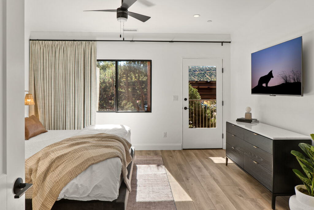 Bedroom with a dresser, wall-mounted TV, and a glass door to the outside