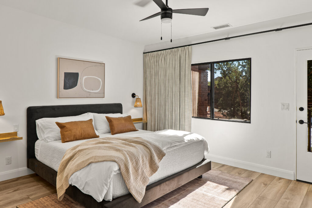 Bedroom with an upholstered bed, a window to the trees, and a door out to the patio