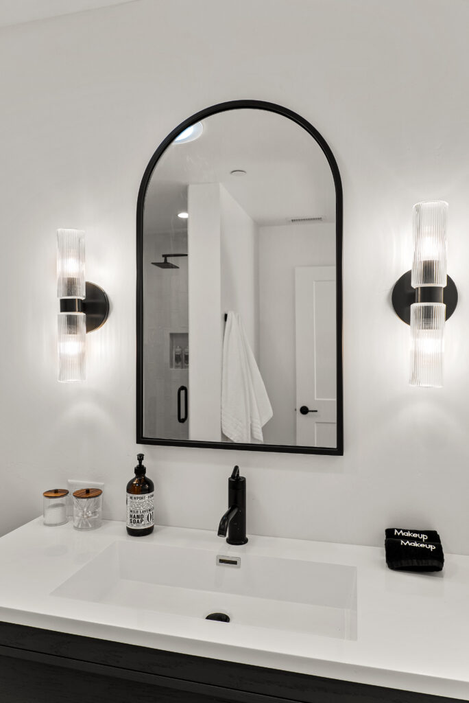 Bathroom mirror flanked by fluted glass sconces, with the shower reflected behind