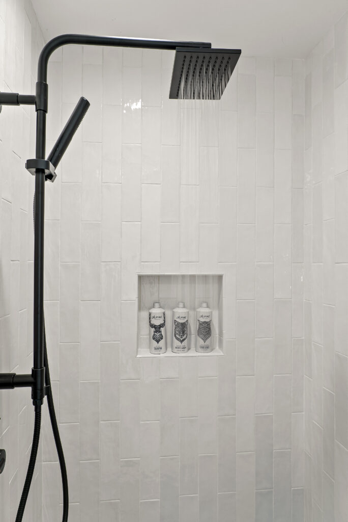 Shower niche with toiletry bottles set into vertically stacked white tile