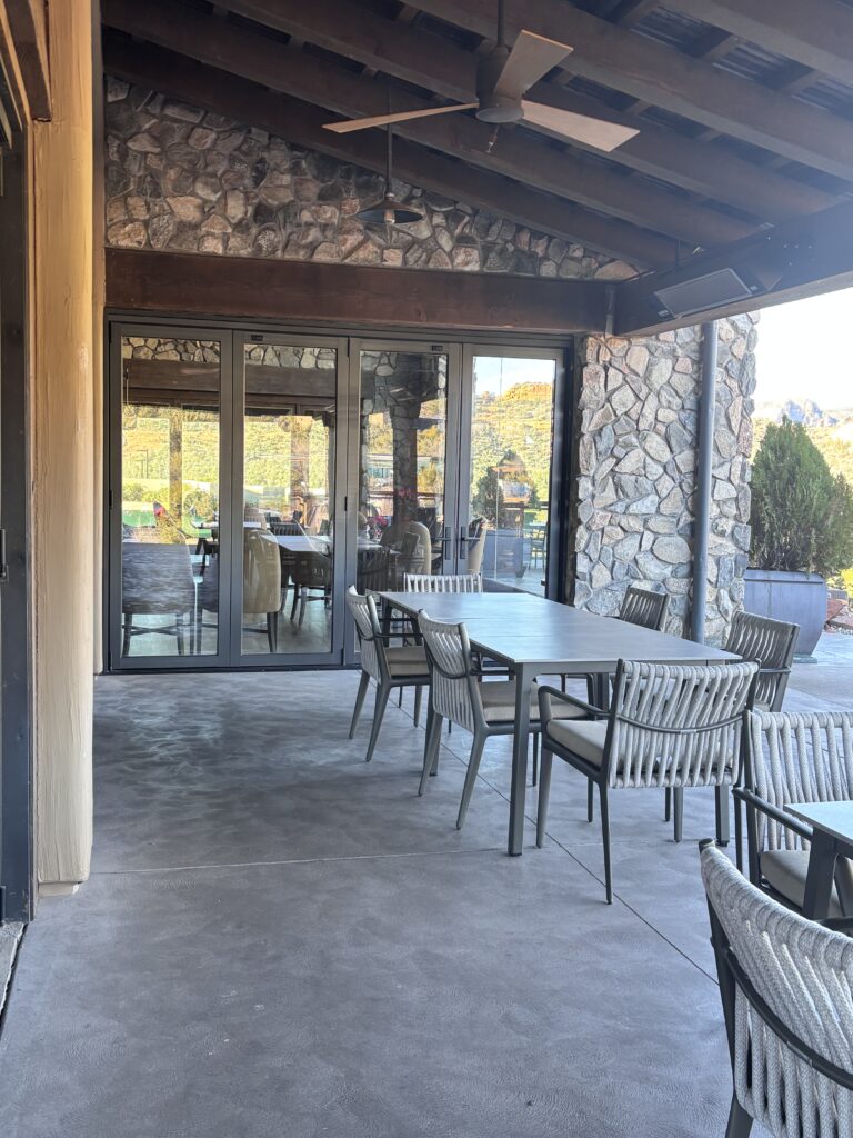 Covered outdoor dining under a timber ceiling, with sliding glass doors open to the dining room