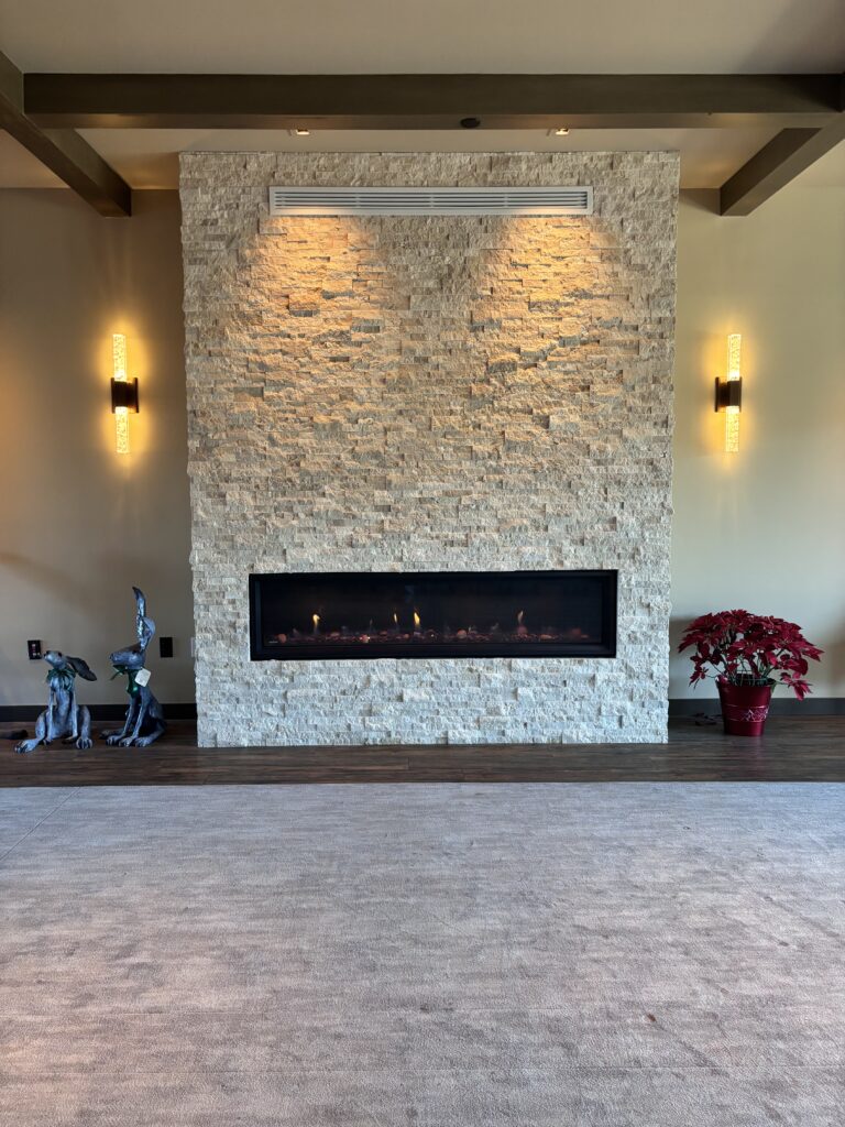 Stacked stone fireplace wall with a linear gas fire and vertical sconces in the clubhouse lounge