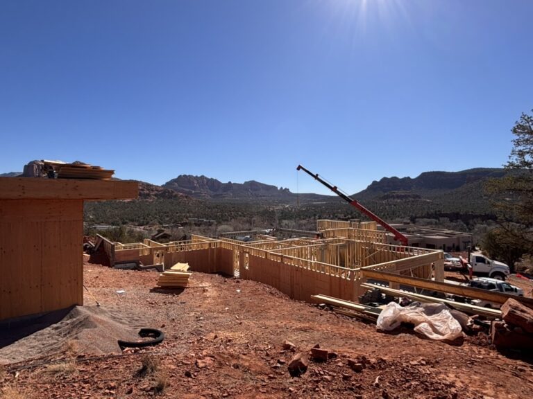 Exterior walls framed and braced on a Kirkwood Builders custom home site near Sedona, Arizona, with a crane working and red rock formations behind