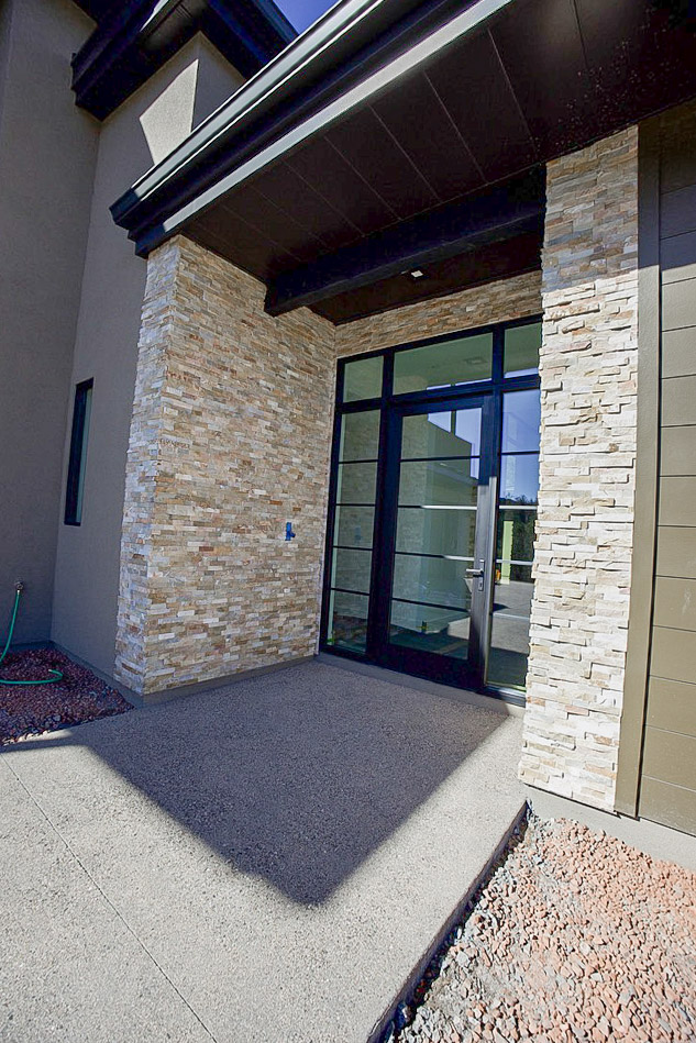 Covered entry with stacked stone columns and black-framed glass doors