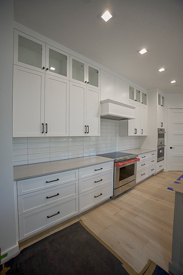 Kitchen run with a vent hood, tile backsplash and wall ovens