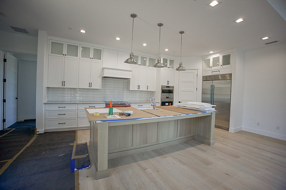Kitchen from the far side, island and pendants with the refrigerator beyond