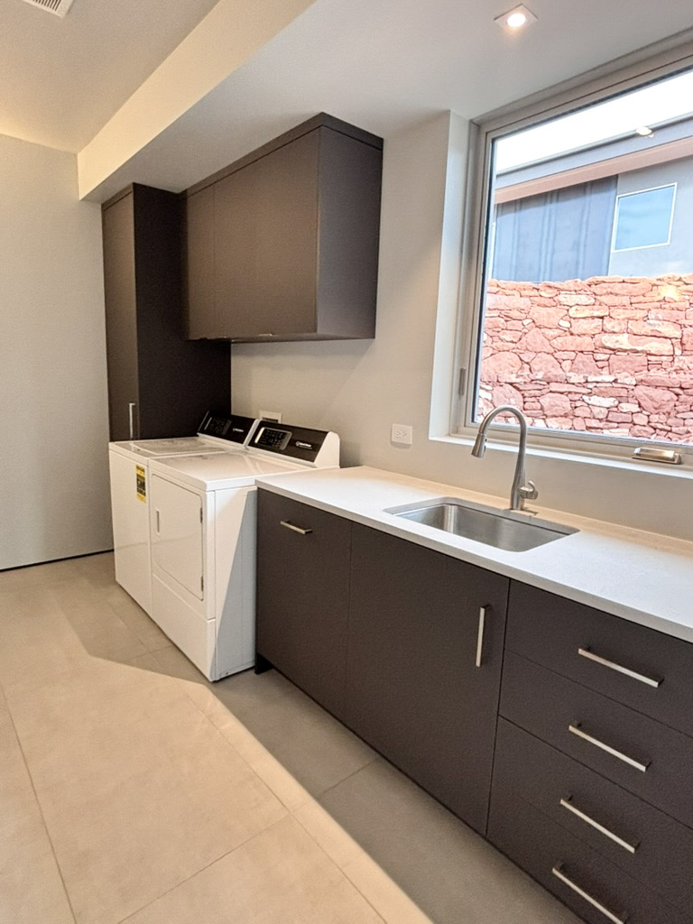Laundry room with machines set under a run of counter, sink and a window