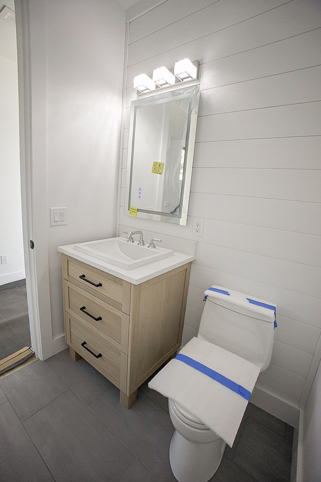 Powder room with a light oak vanity, shiplap wall and black fixtures
