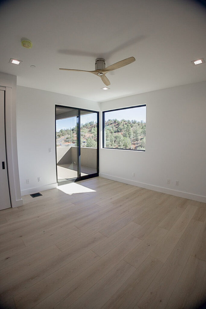 Bedroom with a corner window and slider onto the terrace, junipers beyond
