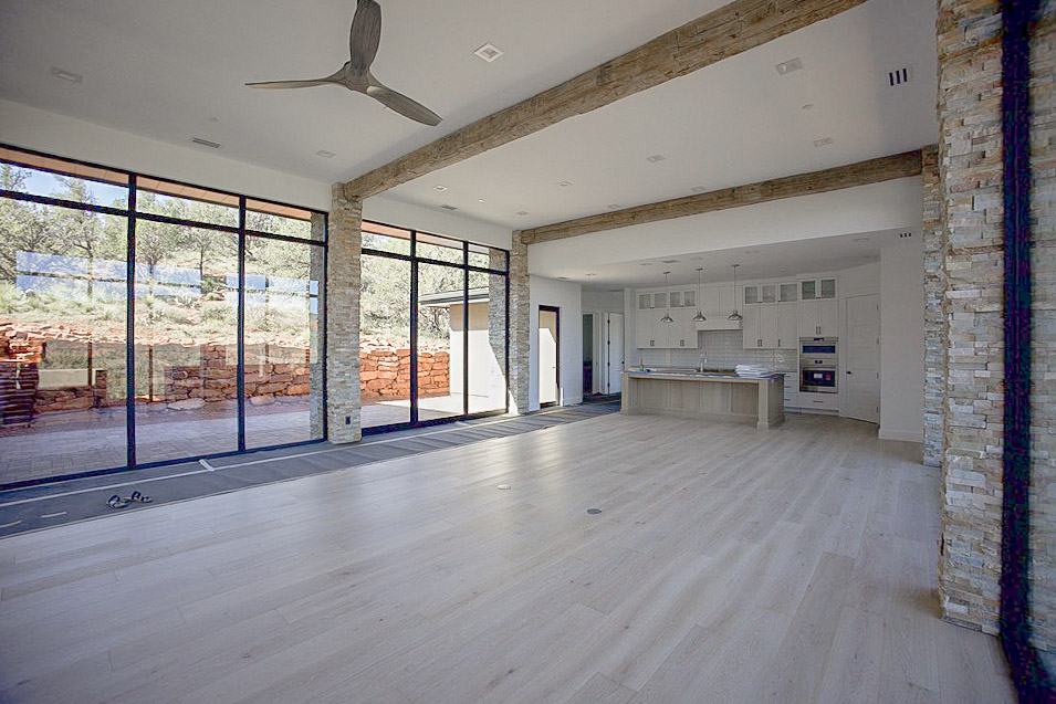 Great room under a timber beam, with a wall of glass and the kitchen beyond